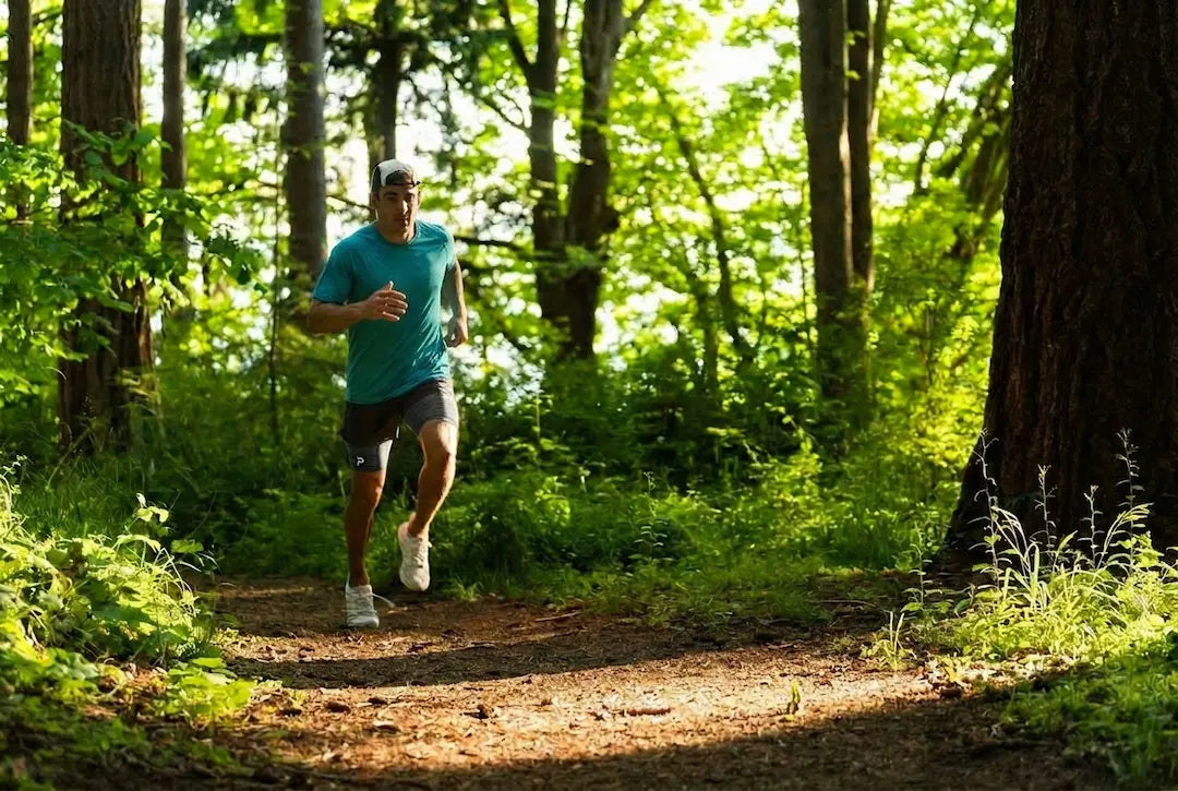 Athlete running on a wooded trail wearing The Draper Performance Tee in teal, highlighting lightweight comfort and performance during outdoor training.
