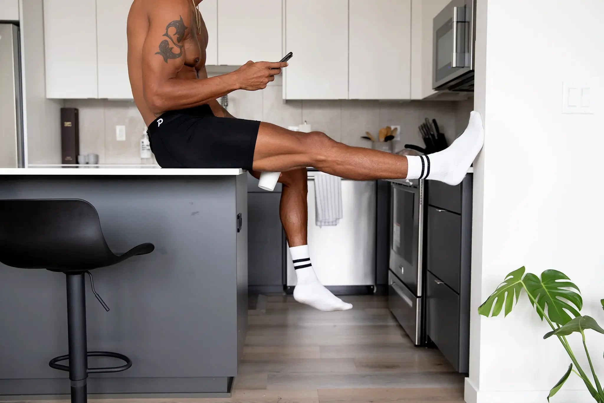 Male athlete sitting on a kitchen counter in black Pacterra Fiver boxer briefs, demonstrating a comfortable, non-binding fit for daily wear and stretching.