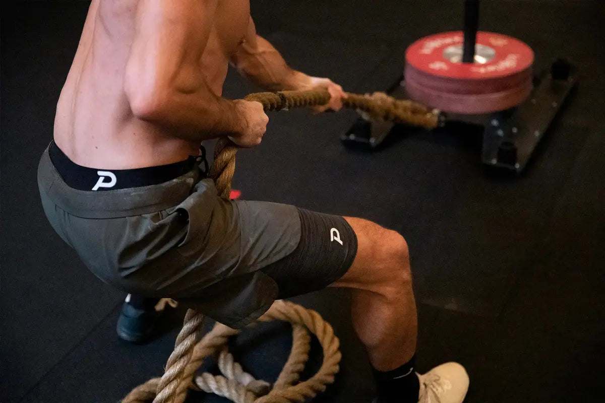 Athlete using battle ropes in black Middy compression shorts, showcasing the durable, anti-chafe fabric.