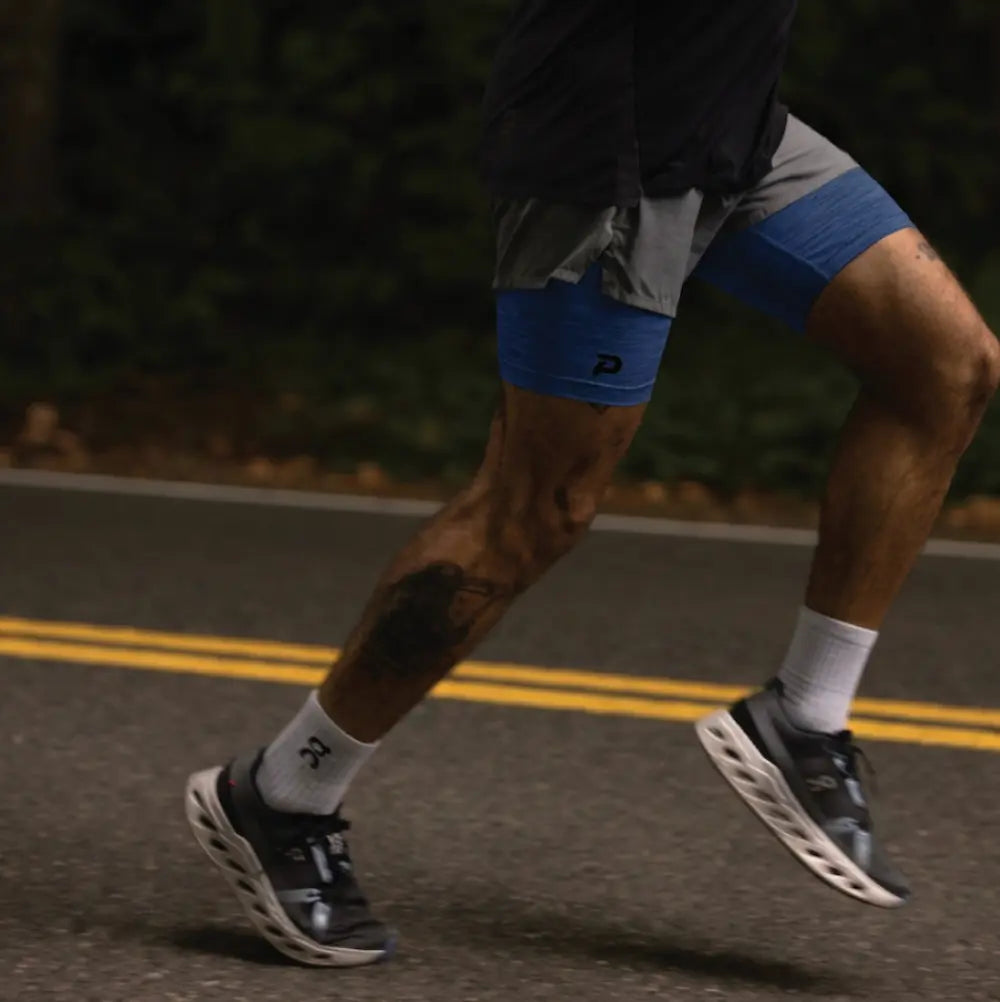 A runner on a road at night wearing navy Pacterra Middy compression shorts as a base layer, demonstrating stability and no-ride-up performance during movement.