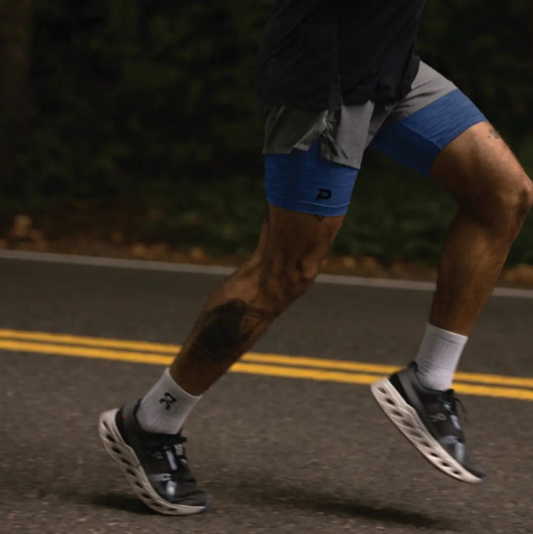 A runner on a road at night wearing navy Pacterra Middy compression shorts as a base layer, demonstrating stability and no-ride-up performance during movement.