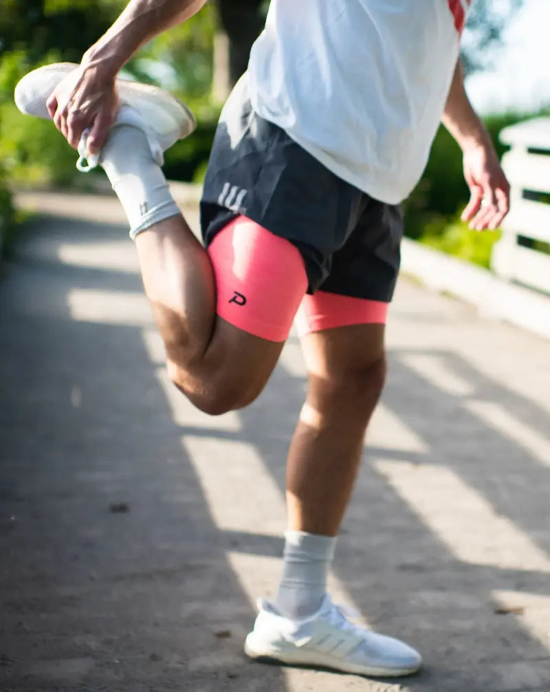 Runner stretching on a path wearing Pacterra Athletics men's compression shorts with a breathable, moisture-wicking compression fabric and a hidden pocket.