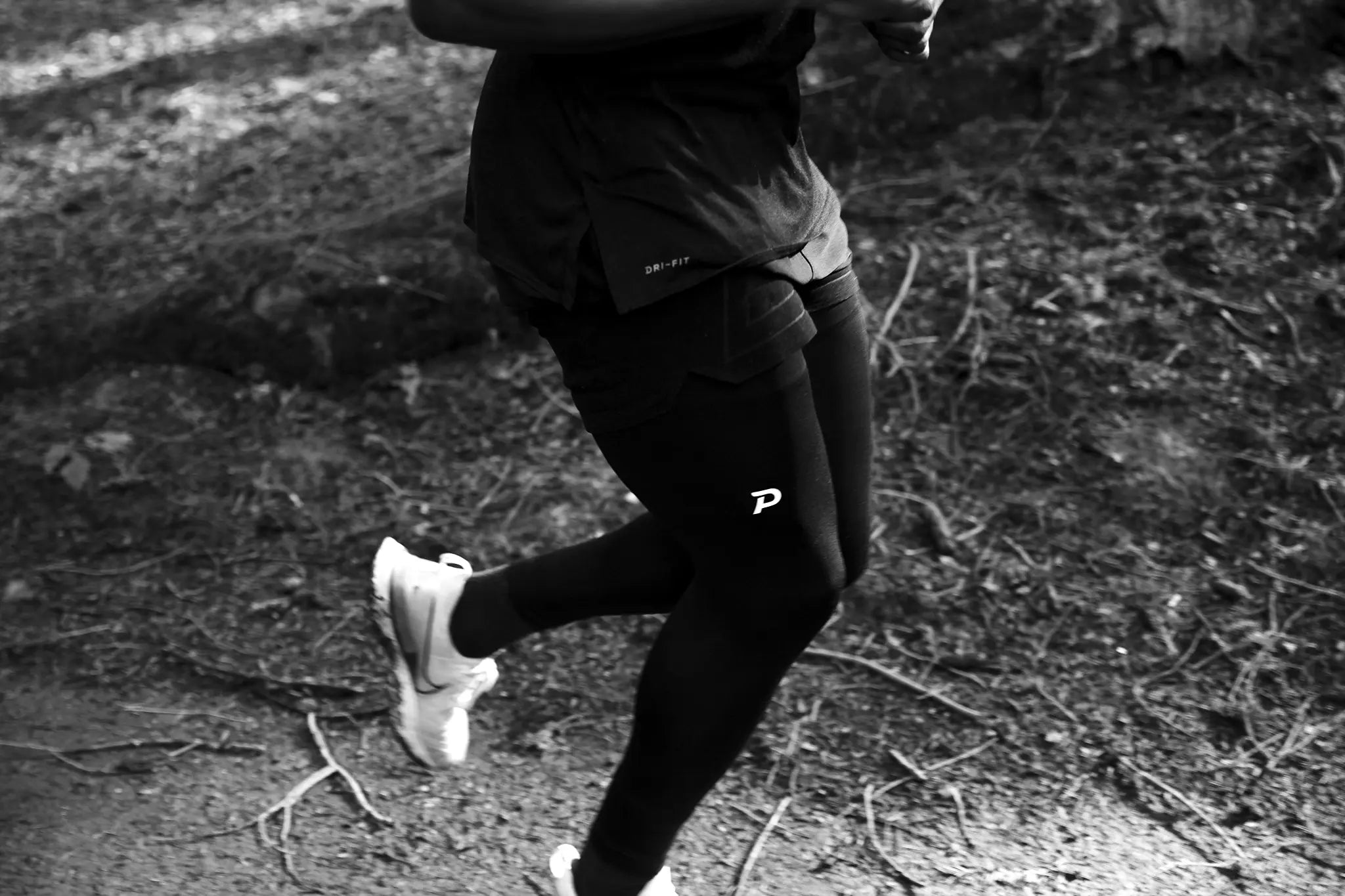 Black and white action shot of a runner on a wooded trail wearing Pacterra mens compression tights with a visible white P logo.