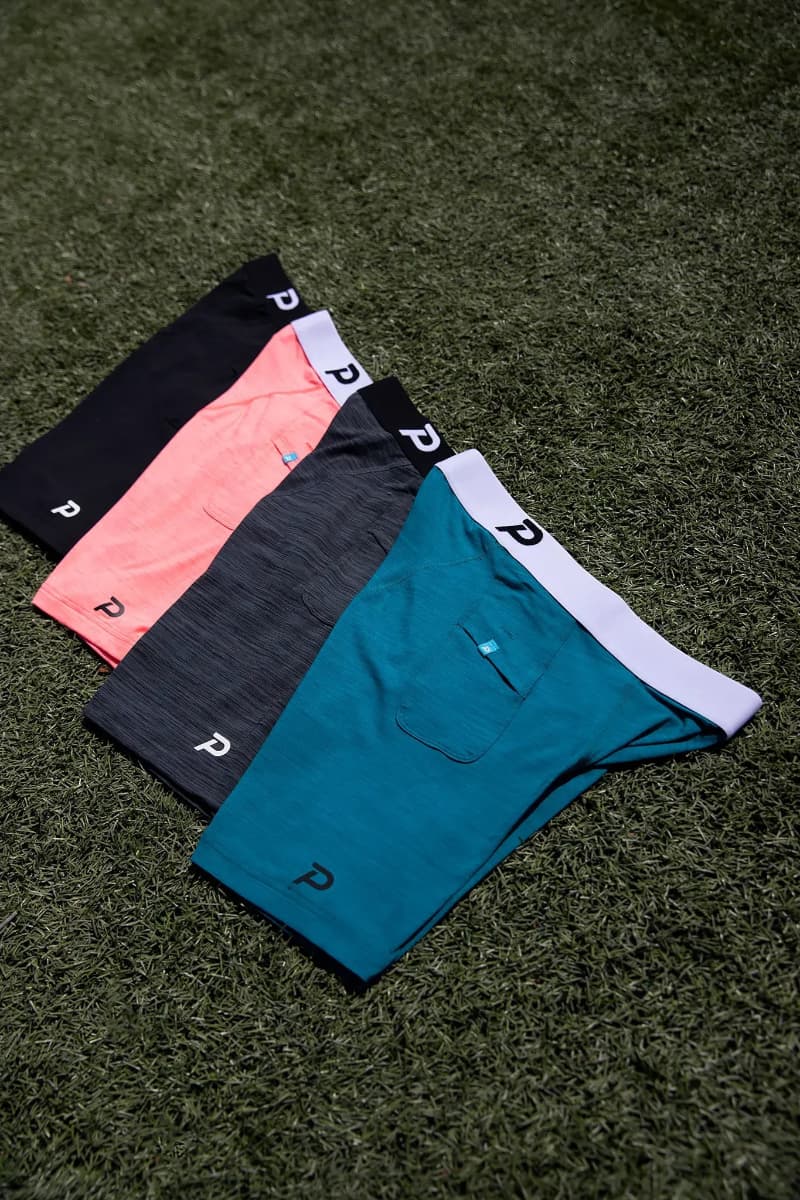 A lineup of Pacterra Men’s Middy Compression Shorts in black, pink, grey, and blue, displayed on an athletic turf background.