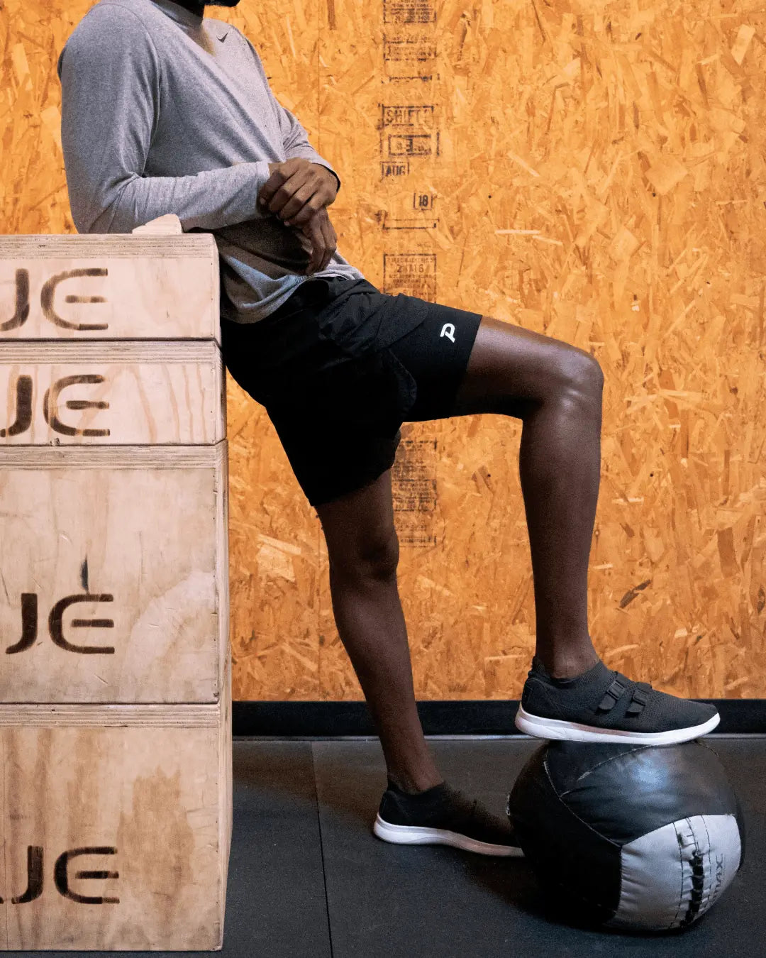 Athlete leaning against a plyo box wearing black Pacterra Middy compression shorts, used as a comfortable gym base layer.