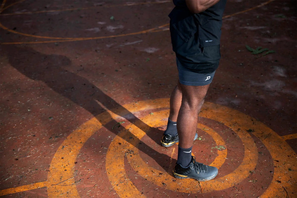 Side view of an athlete on an outdoor court wearing grey Pacterra Middy compression shorts, designed for moisture-wicking performance and muscle support.