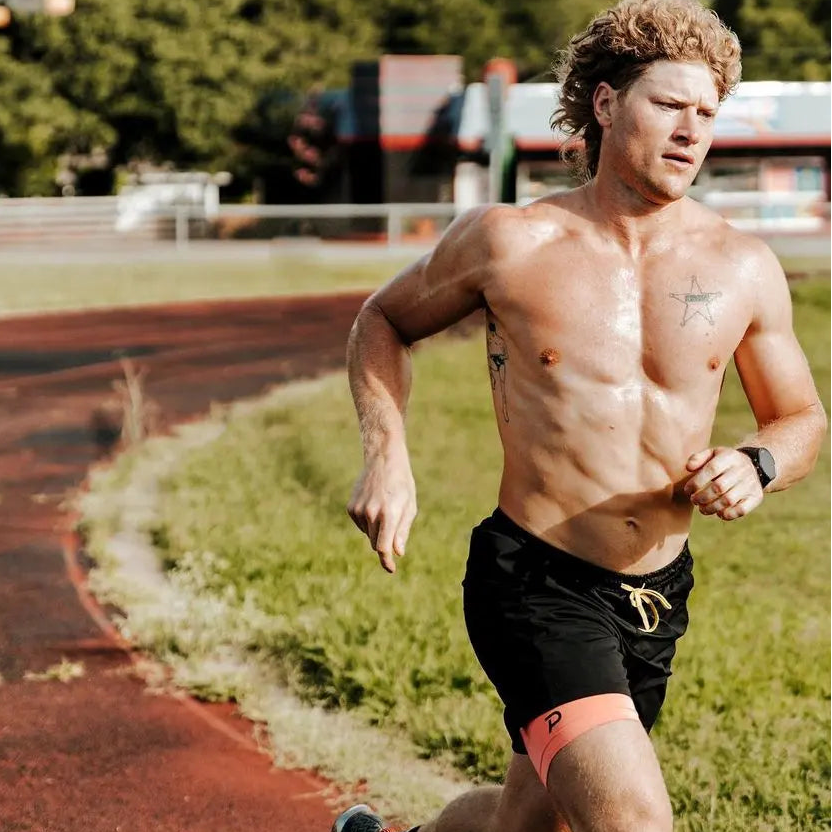 A male athlete sprinting on an outdoor track wearing pink Pacterra Middy compression shorts built to be comfortable and breathable.