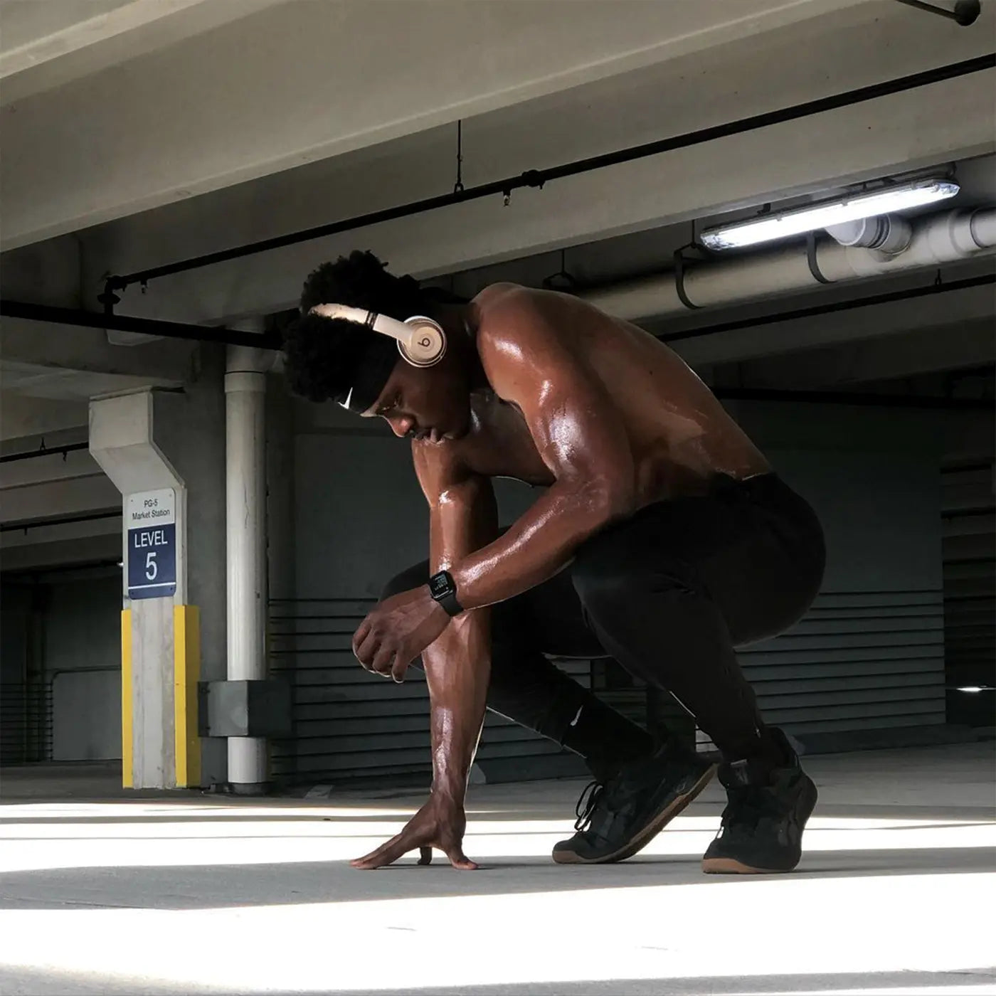 Sweating athlete crouching in a parking garage wearing Pacterra Strider black compression tights and workout gear.
